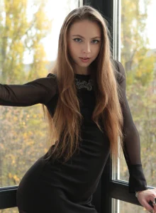 Young girl in long sexy fashion black dress undresses by the window to show her exciting fresh slim body with the nipples stretching and large pussy lips